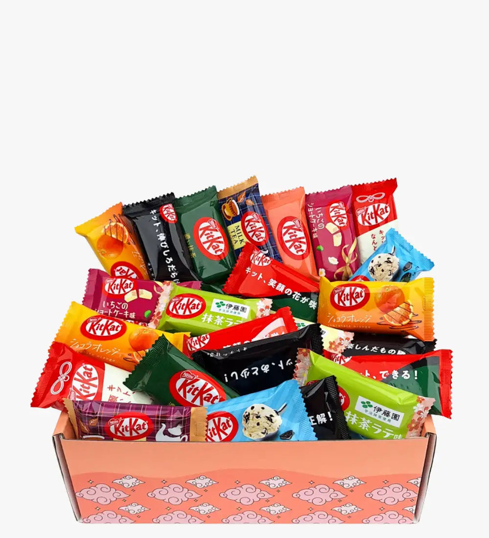 Żywy zestaw batonów czekoladowych KitKat w kolorowych, mieszanych opakowaniach umieszczonych w różowym, wzorzystym pudełku prezentowym.