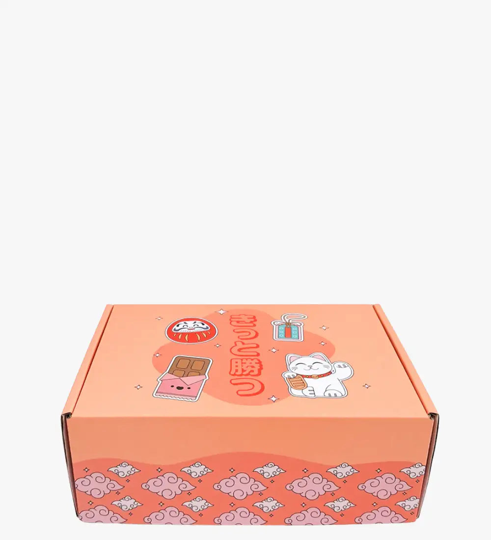 Koralowo-kolorowe pudełko z kartonu z uroczymi japońskimi ilustracjami, w tym białym kotem maneki-neko, daruma i wzorami czekoladowych batonów.